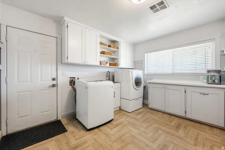 Laundry room featuring herringbone-pattern wood-finish flooring, white cabinetry, a built-in sink, and a large window