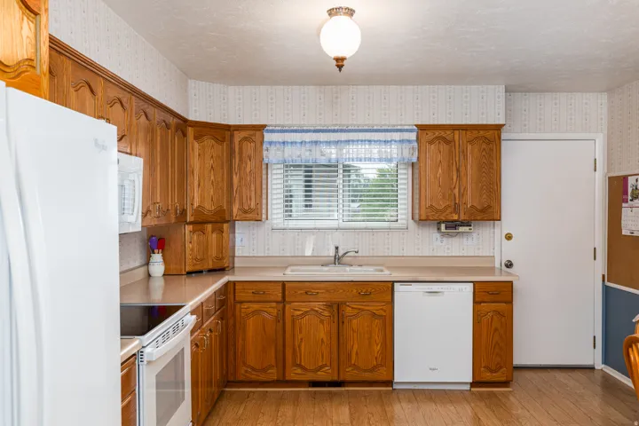Kitchen featuring wood-finish flooring, wood cabinetry, built-in white appliances, and a window above the sink