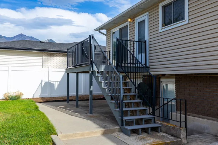 Exterior featuring beige siding, a raised deck with black metal railings, and a concrete patio