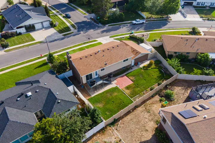 Expansive backyard with a manicured lawn, red paver patio, and white privacy fencing