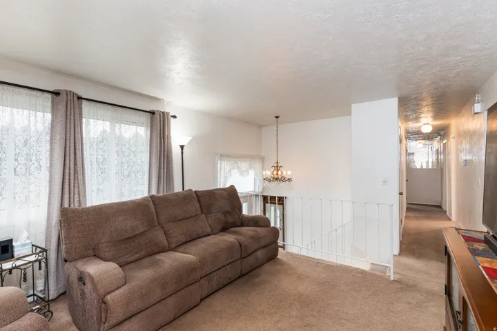 Spacious living room with rolled-arm sofa, neutral carpet flooring, and abundant natural light from dual large windows with fabric drapery