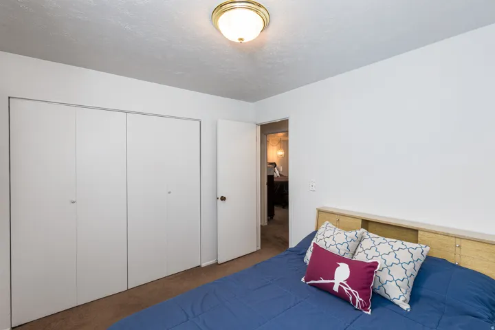 Bright secondary bedroom featuring warm wood-finish flooring, a wood-frame bed with upholstered headboard, and ample natural light from ceiling-mounted fixtures