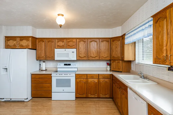 Kitchen featuring wood-finish cabinetry, white appliances, dual basin sink, and wood-finish flooring