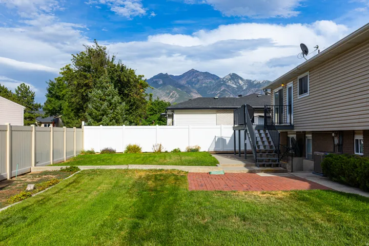 Expansive backyard featuring a green lawn, red brick patio, and a multi-level deck with stairs
