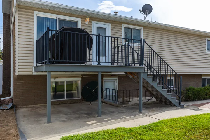 Second-story deck with dark metal railings, providing outdoor access via sliding glass doors and an exterior staircase to a concrete patio