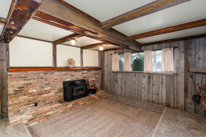 Rustic bedroom retreat showcasing exposed wooden beam ceiling with coffered details, brick fireplace with black surround, wood-paneled walls, and carpet flooring