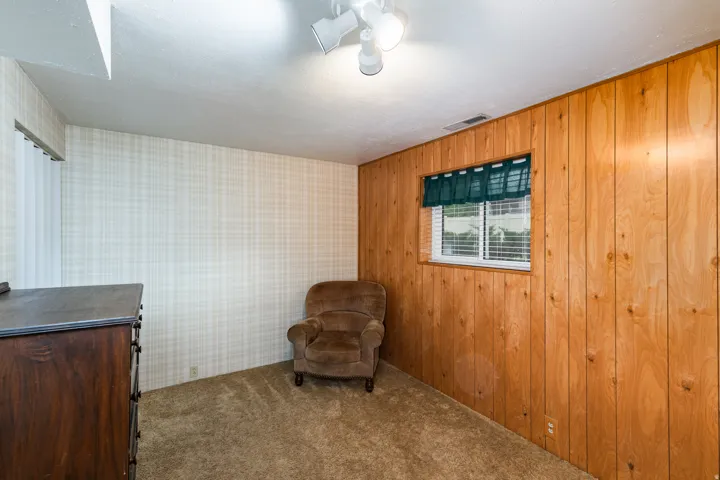 Versatile bonus room featuring warm wood-finish wall paneling, carpeted flooring, and a single-hung window with operable shutters