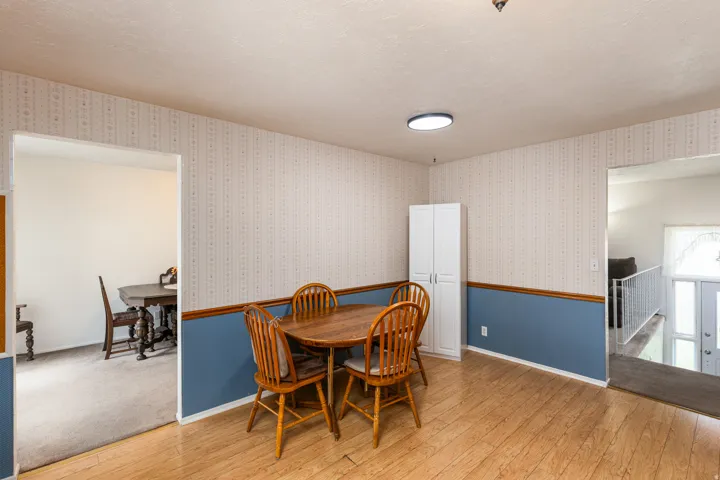Spacious dining area with wood-finish flooring, two-tone walls featuring blue wainscoting and cream upper panels, and recessed ceiling lighting