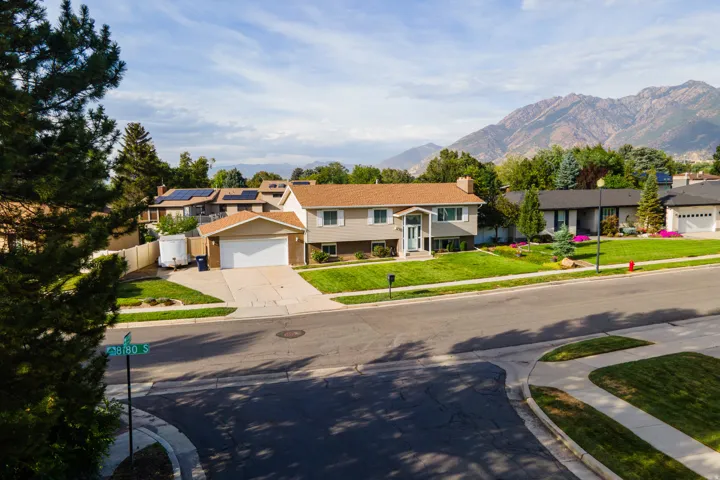 Charming two-story residence featuring a tan exterior with peaked roofline, situated on a manicured lawn with mature landscaping