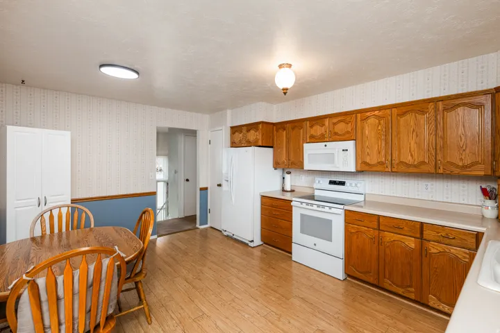 Wood-finish flooring, wood cabinetry, white appliances, and a built-in pantry