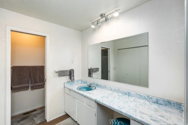 Spa-inspired primary bathroom showcasing a marble-look countertop with dual sink vanity, large framed mirror with integrated lighting, and direct access to the ensuite