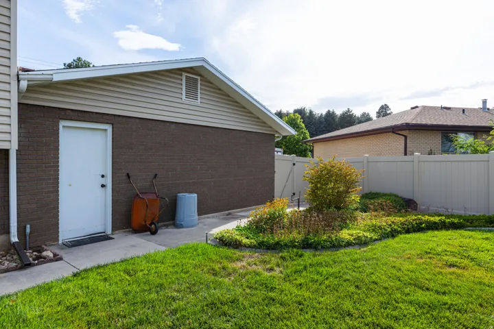 Exterior structure featuring brick and siding, a side entry door, a manicured lawn, established landscaping, and a privacy fence