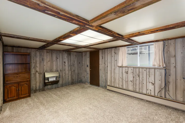 Carpeted room featuring wood-paneled walls, a wood-beamed ceiling with recessed lighting, and a built-in wall heater