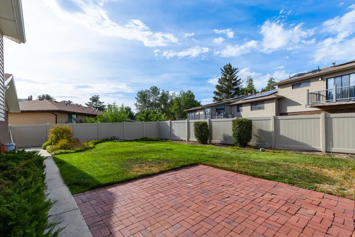 Enclosed backyard featuring a red brick paver patio, a green lawn, and a light-toned privacy fence