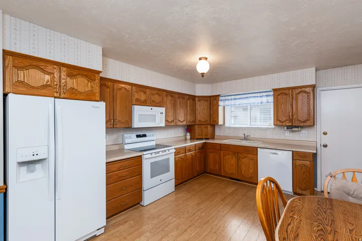 Functional kitchen featuring wood-finish cabinetry, white appliances, laminate countertops, and wood-finish flooring