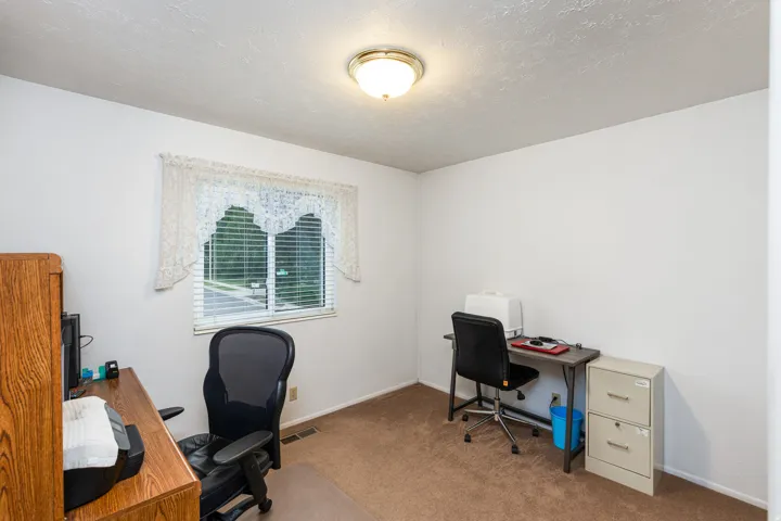 Dedicated home office featuring carpeted flooring, dual workstations with built-in desk surfaces, ample natural light from a multi-pane window with interior shutters, and recessed ceiling lighting