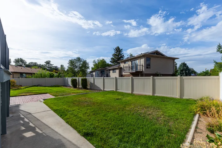 Expansive backyard featuring a manicured lawn, concrete pathway, and a brick patio area