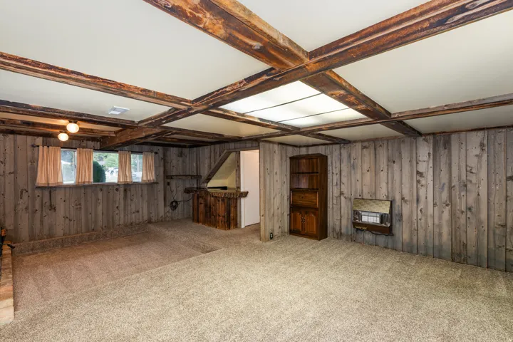 Spacious basement featuring exposed wood beam ceiling with skylight panels, wood-paneled walls, carpeted flooring, and multiple wooden doorways providing access to adjoining spaces