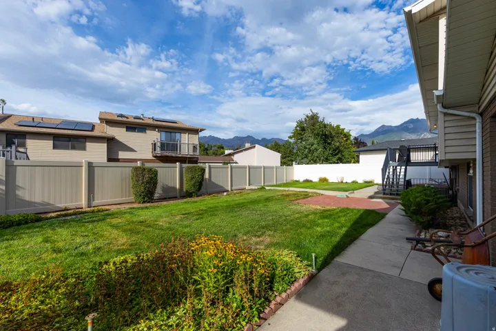 Expansive lawn area with concrete pathway, mature landscaping, and a privacy fence