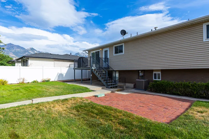 Expansive backyard featuring a brick paver patio, a raised deck with metal stairs, and a white vinyl fence