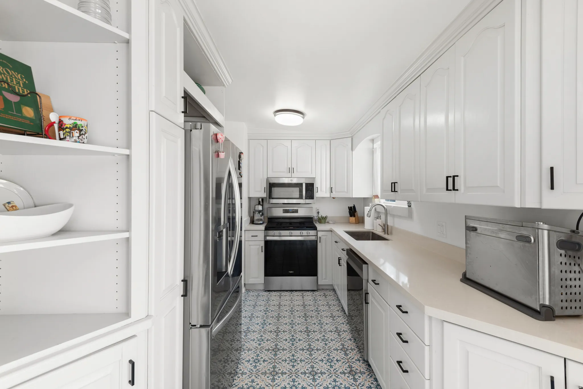 Galley kitchen with white cabinetry, stainless steel appliances, light-toned quartz countertops, and patterned floor tiles