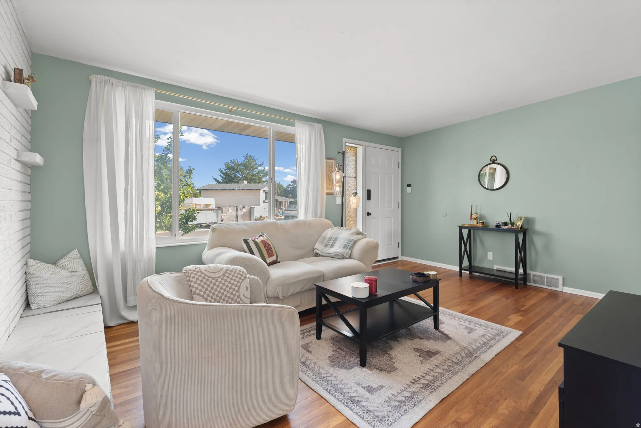 Hardwood flooring, large picture window, painted accent wall, white entry door, and built-in shelving