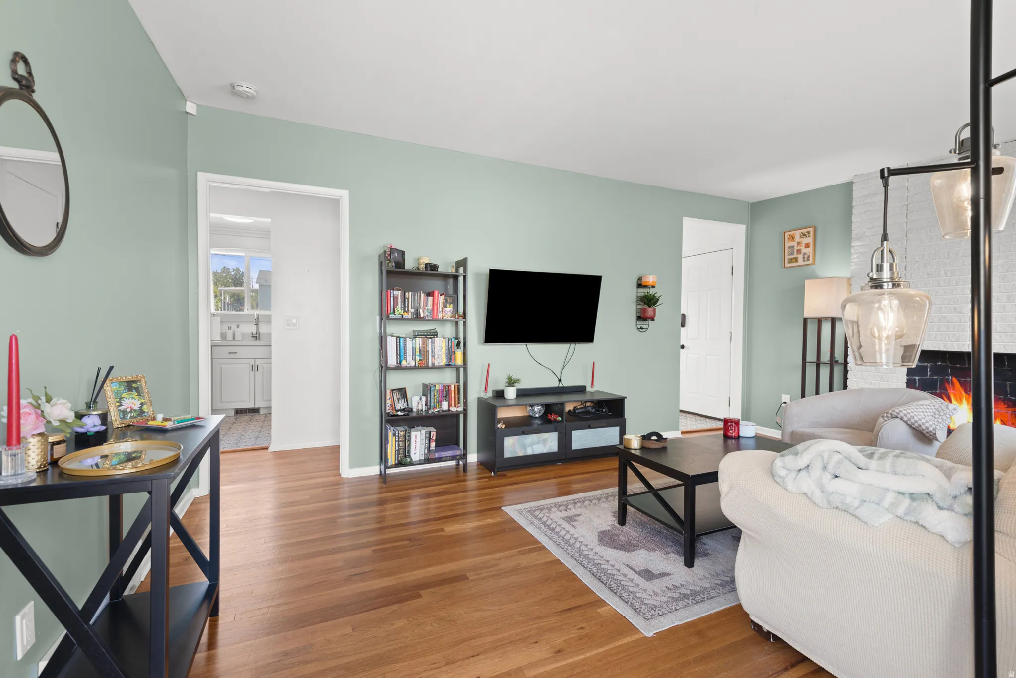 Hardwood-finish flooring, white brick fireplace, and a light green wall palette