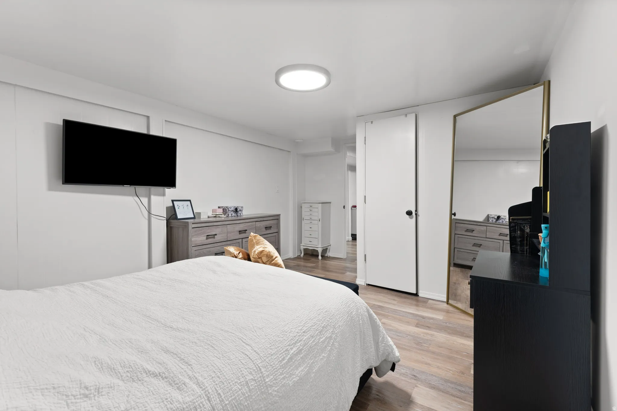 Wood-finish flooring, a ceiling-mounted light fixture, and a wall-mounted television