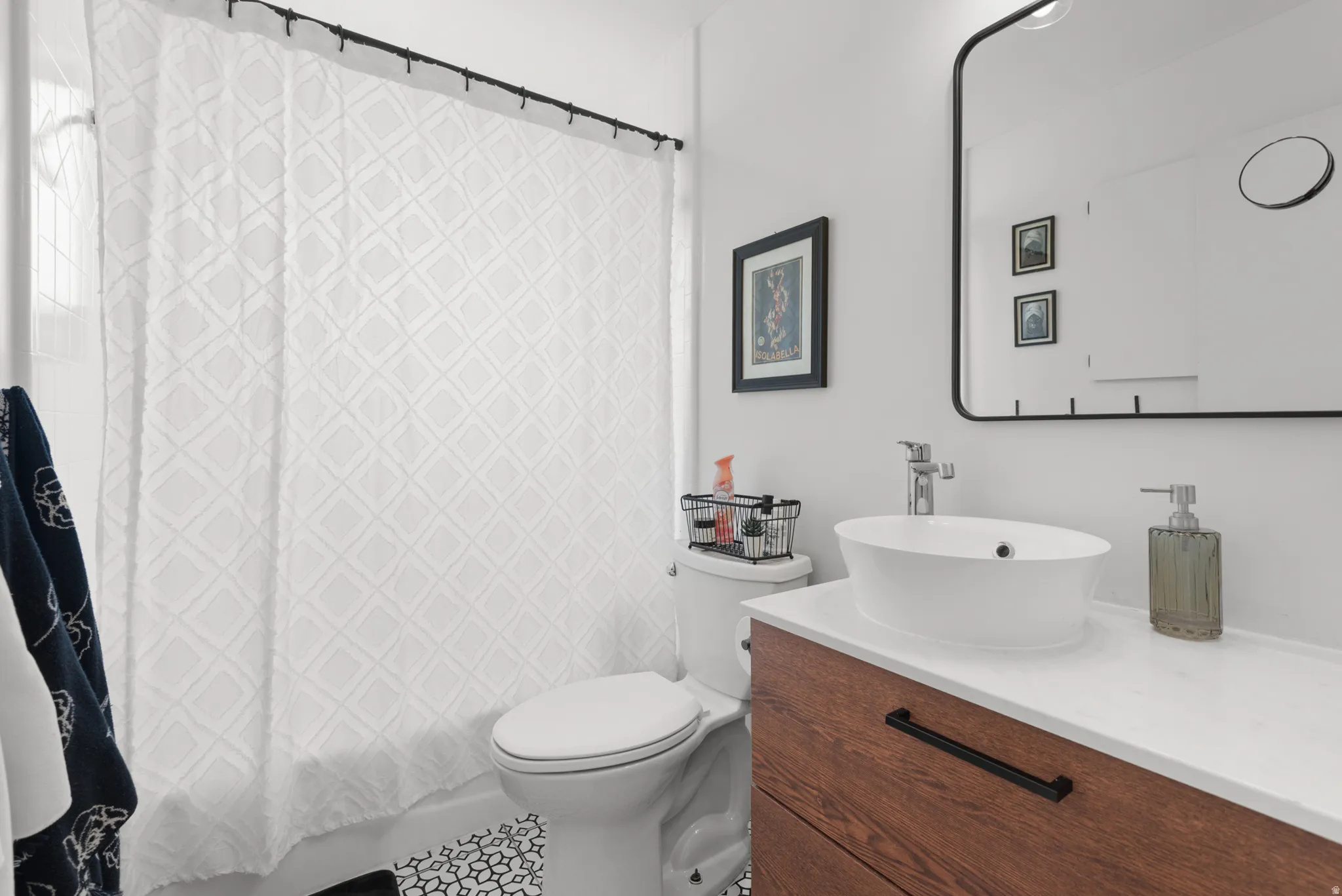Bathroom featuring a wood-finish vanity with a vessel sink, a large wall-mounted mirror, and decorative floor tiling