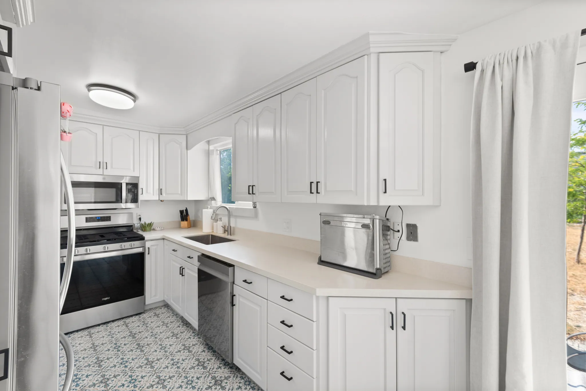 Kitchen featuring white cabinetry, light-toned countertops, stainless steel appliances, patterned floor tile, and recessed lighting