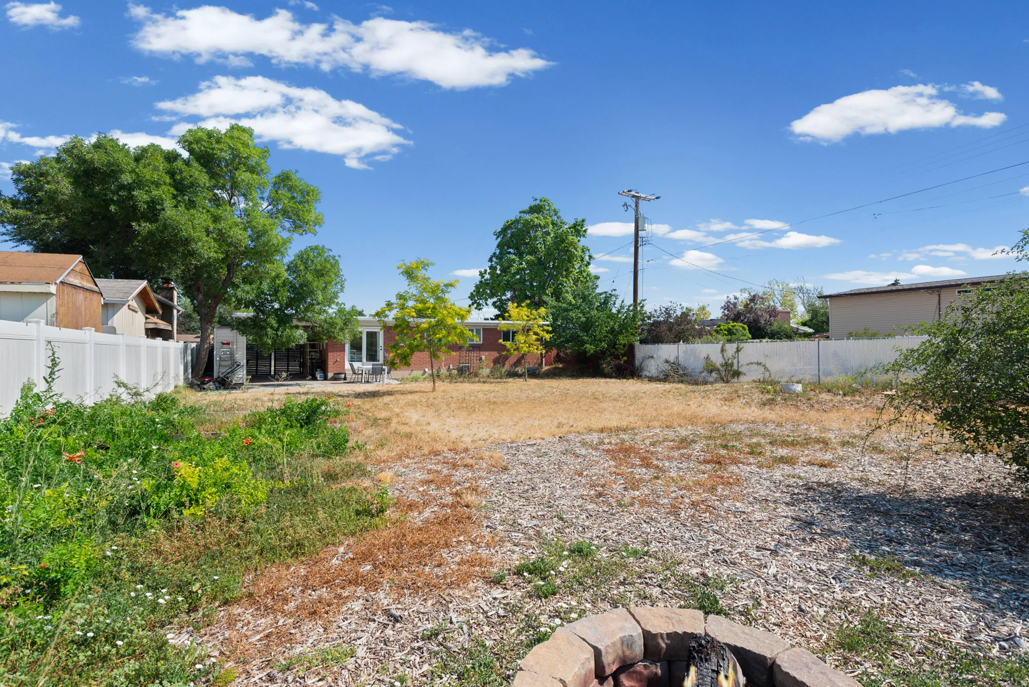 Expansive rear yard featuring mature trees, a privacy fence, and a stone fire pit