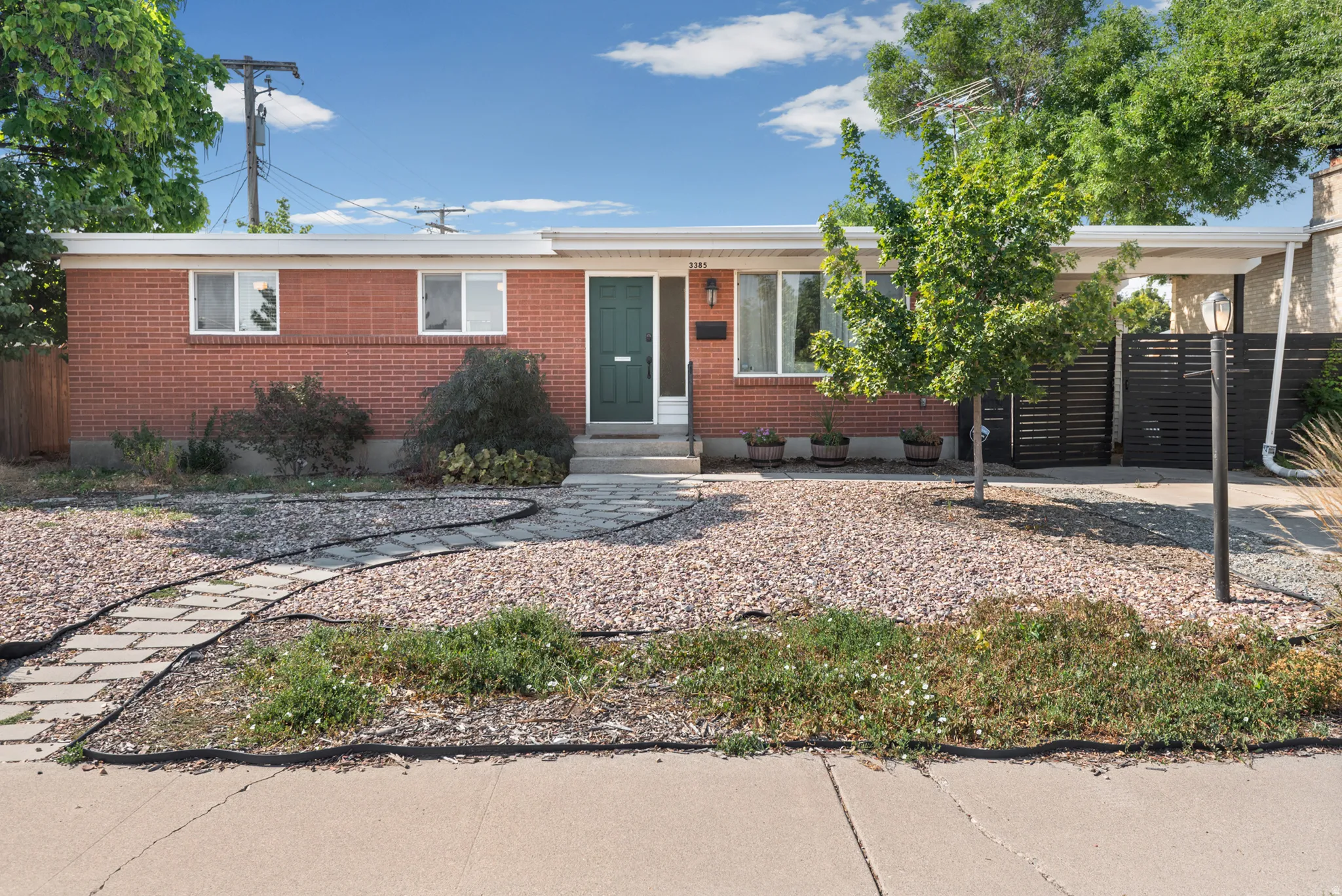 Brick exterior with a dark green entry door, covered carport entry, and a stone pathway.