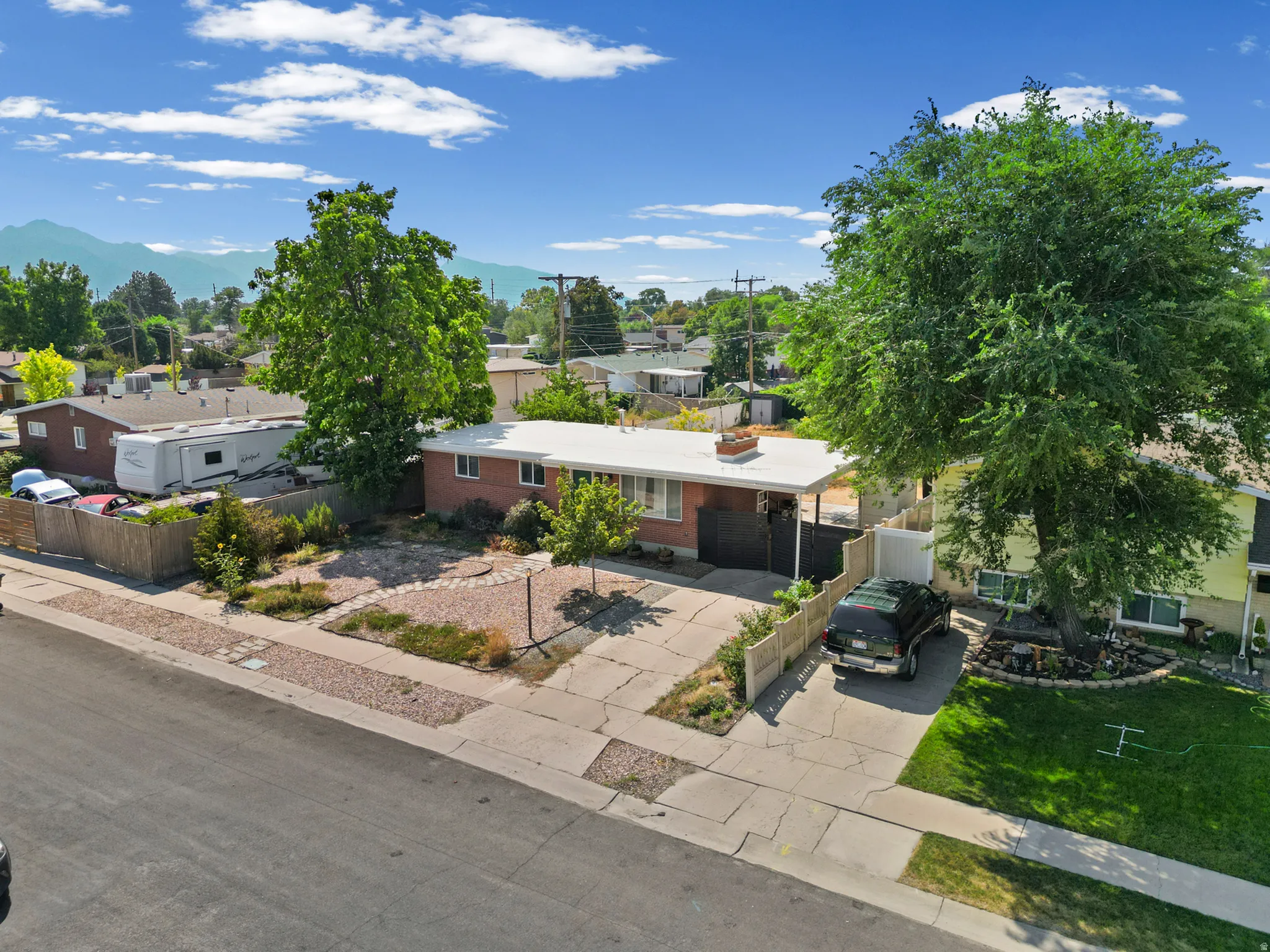 Brick exterior with a white flat roofline, mature trees, a paved driveway, and a fenced yard