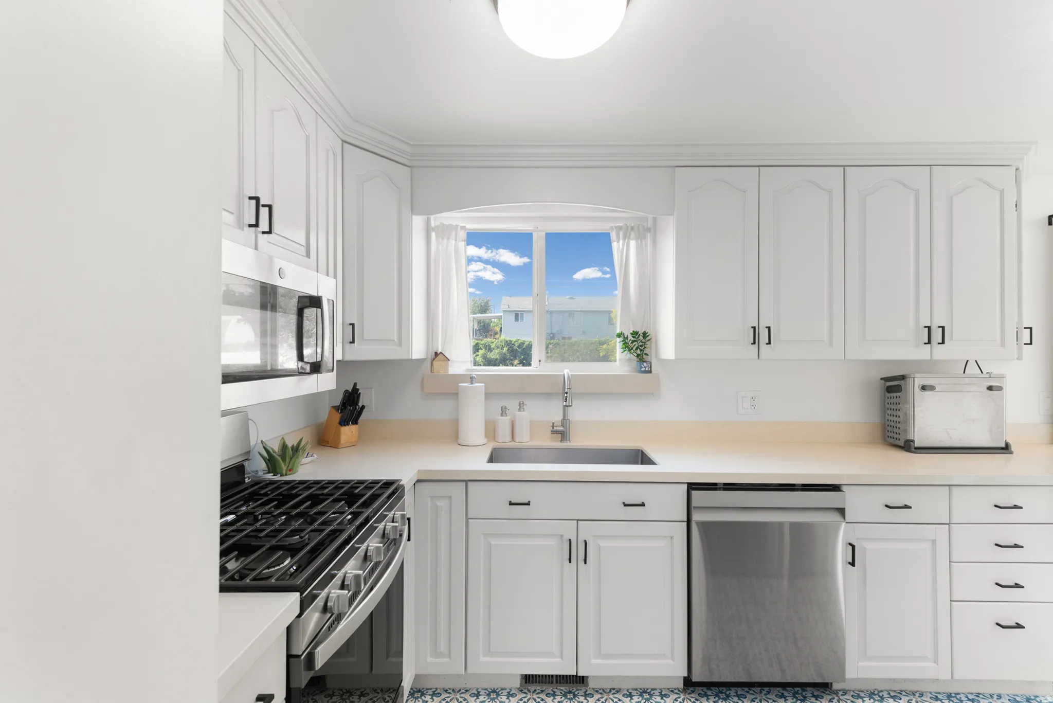 White cabinetry with matte black hardware, stainless steel appliances, with gas stove and light-toned countertops, and a stainless steel sink