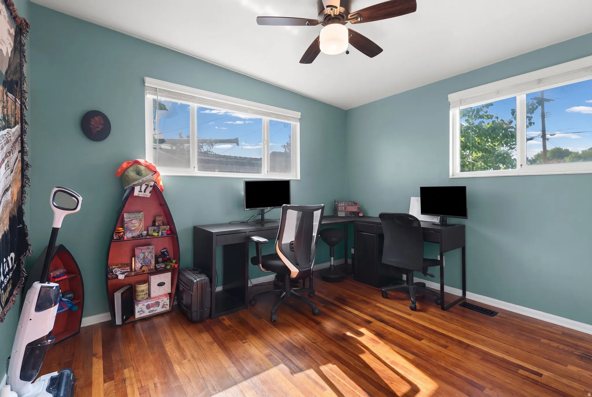 Wood-finish flooring, two windows with blinds, a ceiling fan with integrated lighting, and painted walls