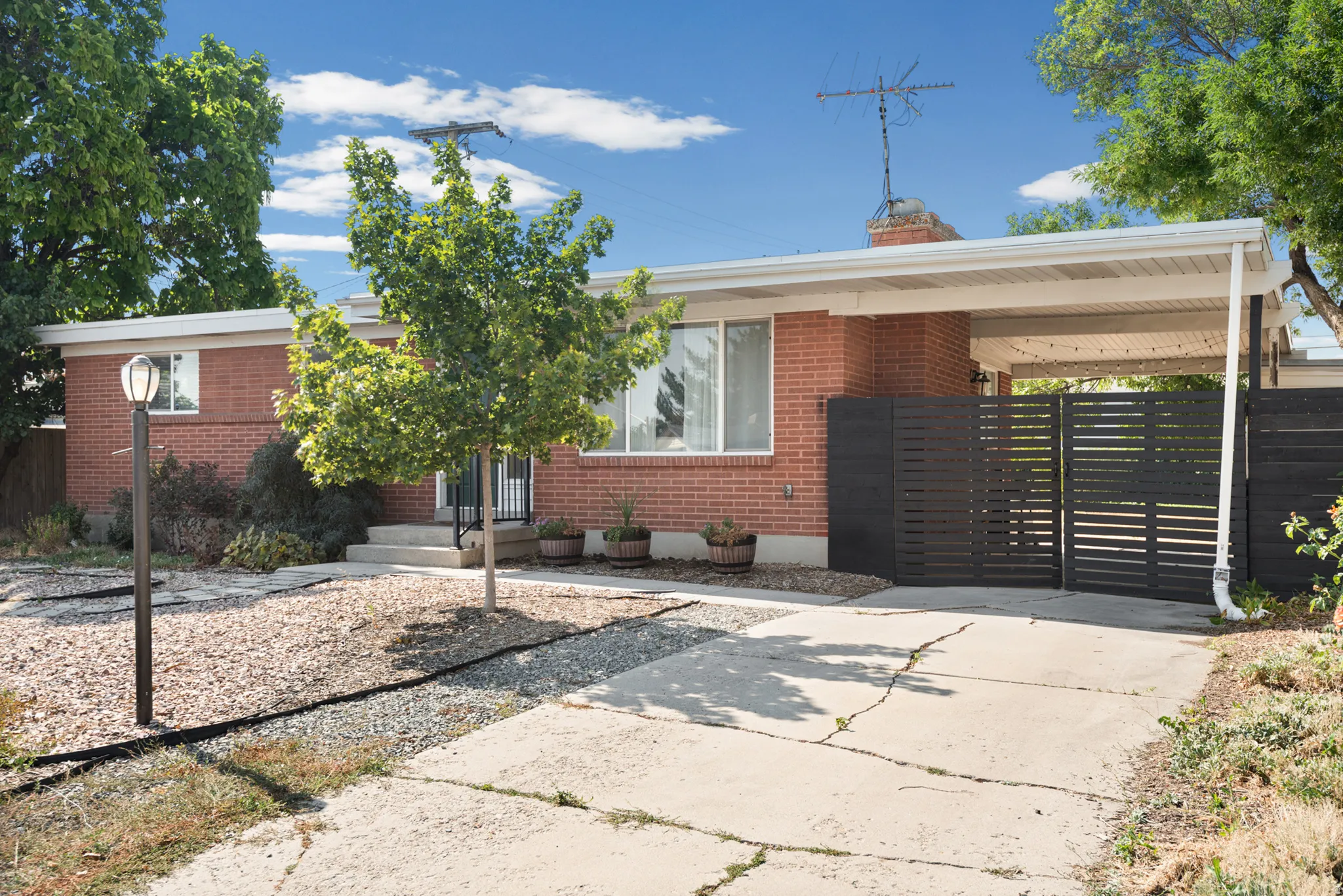 Brick exterior with white trim, covered carport, private slatted gate, and a paved driveway with plenty of space.
