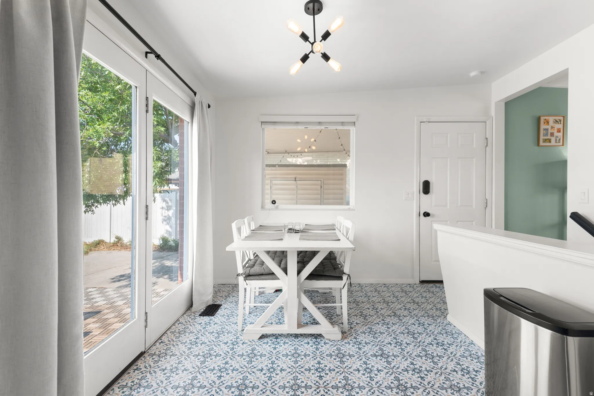 French doors providing outdoor access, patterned floor tiling, a modern ceiling light fixture, a paneled entry door, and a half-wall partition