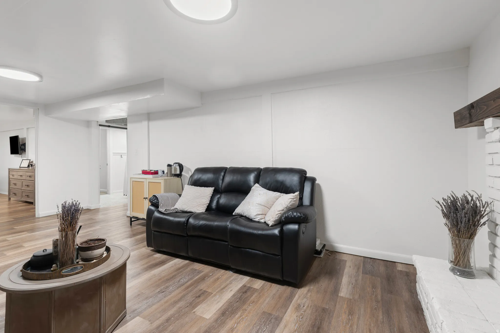 Wood-finish flooring, white painted brick fireplace with wood mantel, recessed lighting, and white walls