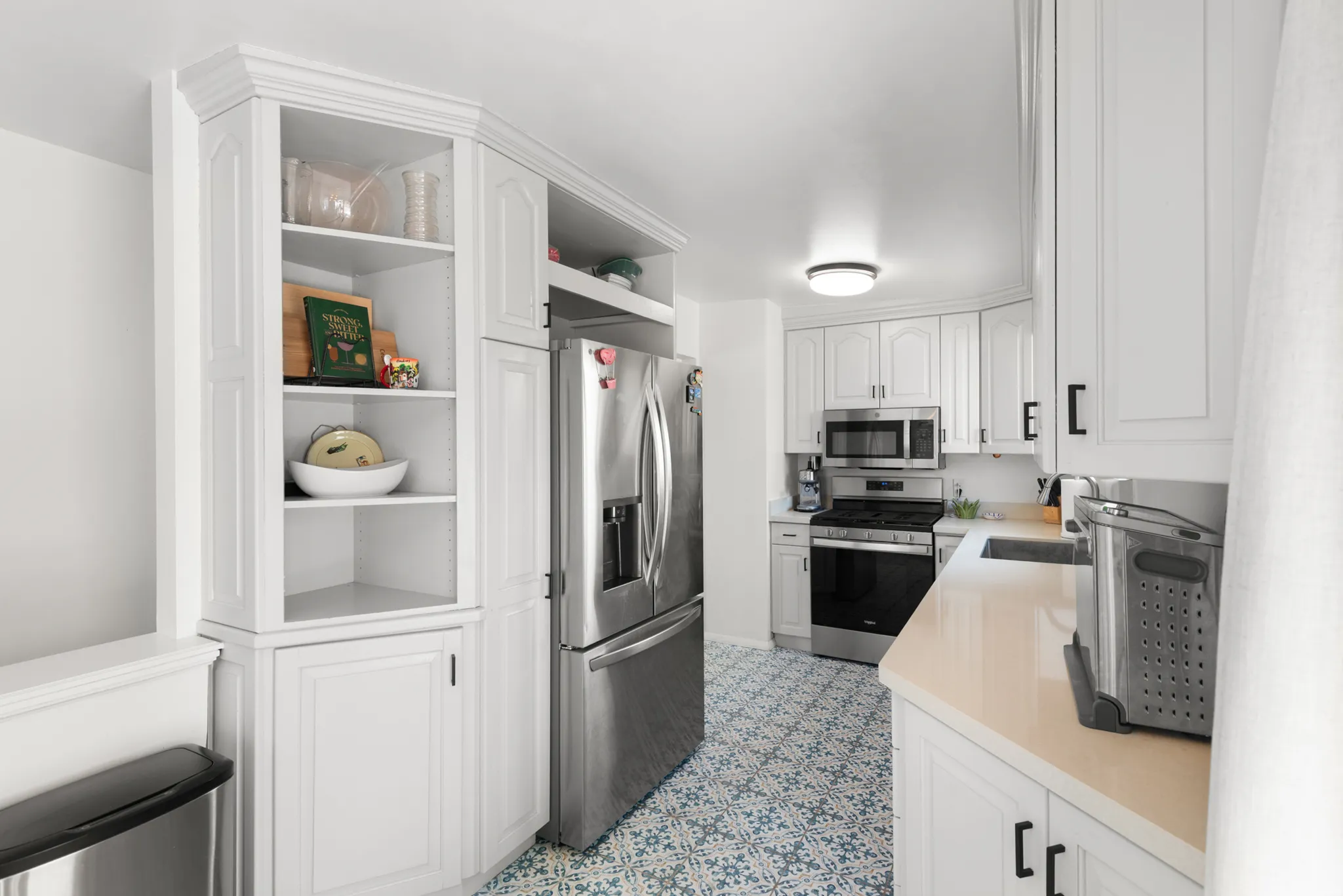 White cabinetry with black hardware, stainless steel appliances, patterned floor tile, built-in shelving, and light-toned countertops