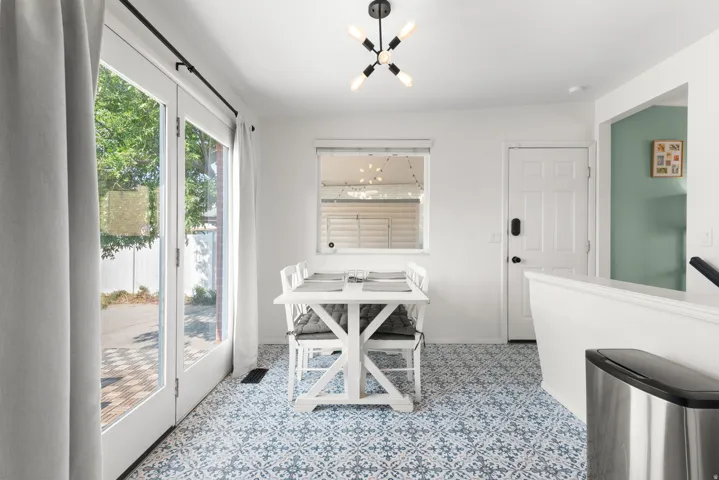 French doors providing outdoor access, patterned floor tiling, a modern ceiling light fixture, a paneled entry door, and a half-wall partition
