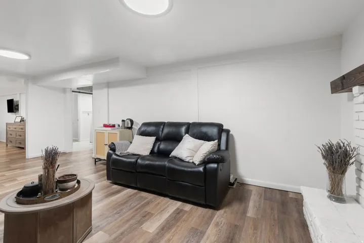 Wood-finish flooring, white painted brick fireplace with wood mantel, recessed lighting, and white walls