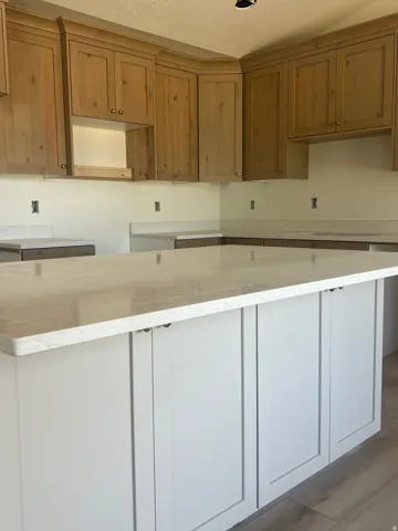 Modern kitchen featuring warm wood-finish cabinetry with shaker-style doors, a substantial center island with white painted base and light quartz countertop, stainless steel appliances, and crisp white subway tile backsplash with coordinating grout lines