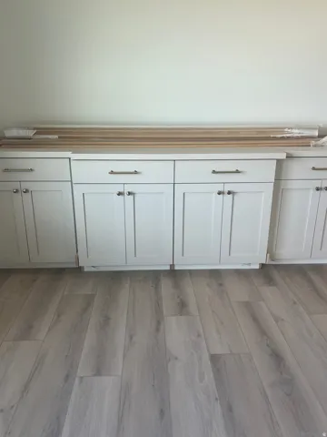 White Shaker-style cabinetry with brushed nickel hardware, light-toned countertops, and wood-finish flooring