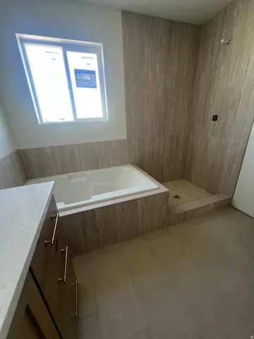 Built-in bathtub with surrounding tile, separate tiled shower, and a wood-finish vanity with a light-toned countertop