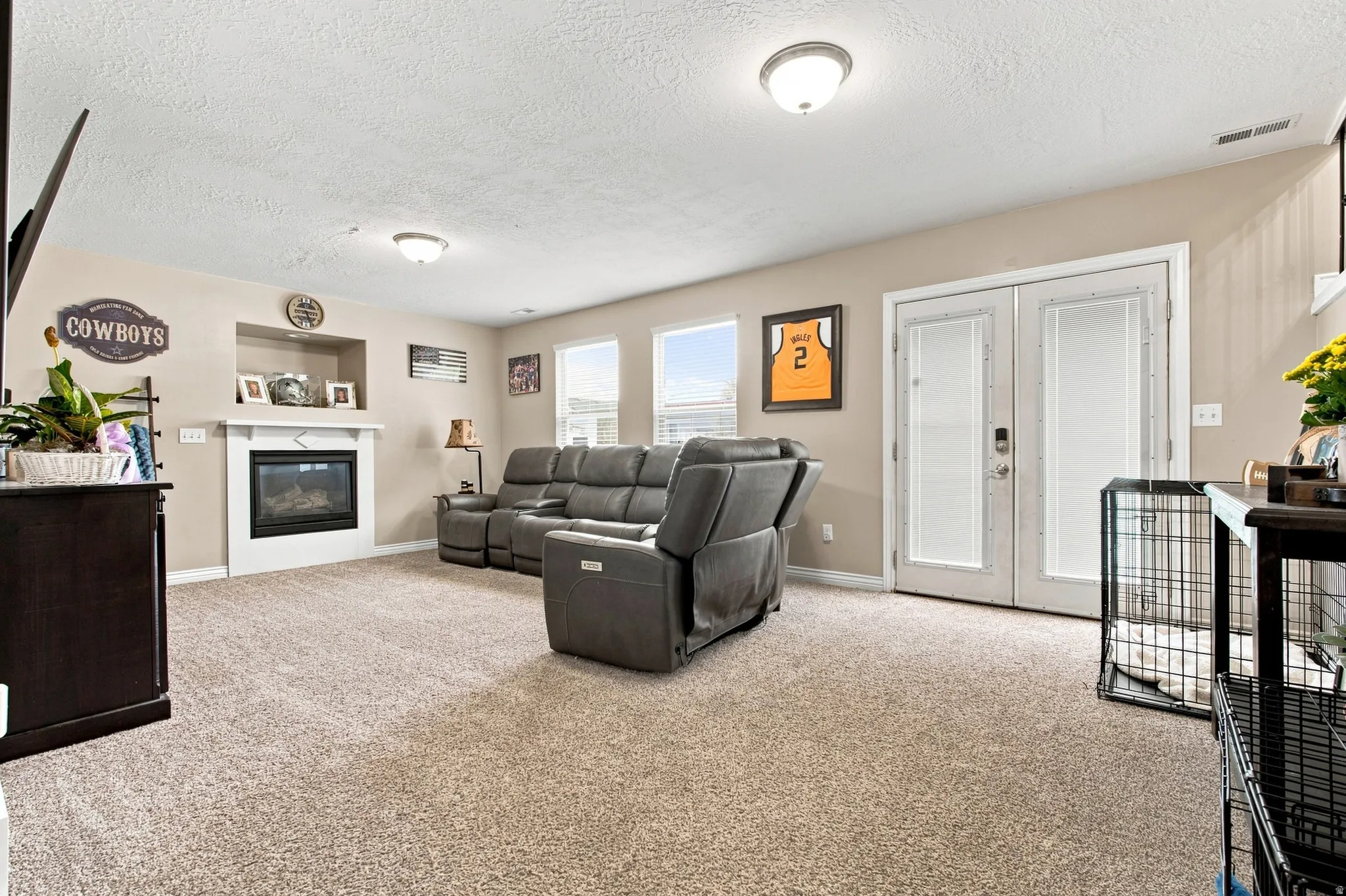 Recessed gas fireplace with a mantel, multiple windows, French doors with frosted glass, and neutral-toned carpeting