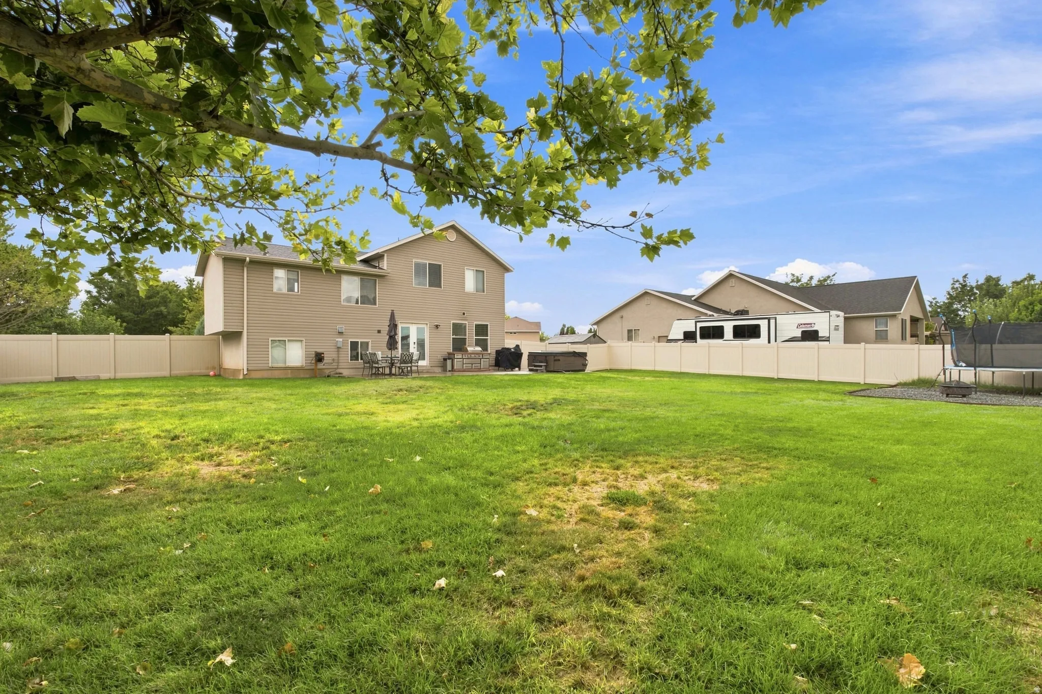 Expansive grassy yard with full perimeter fencing, patio space, and a built-in hot tub