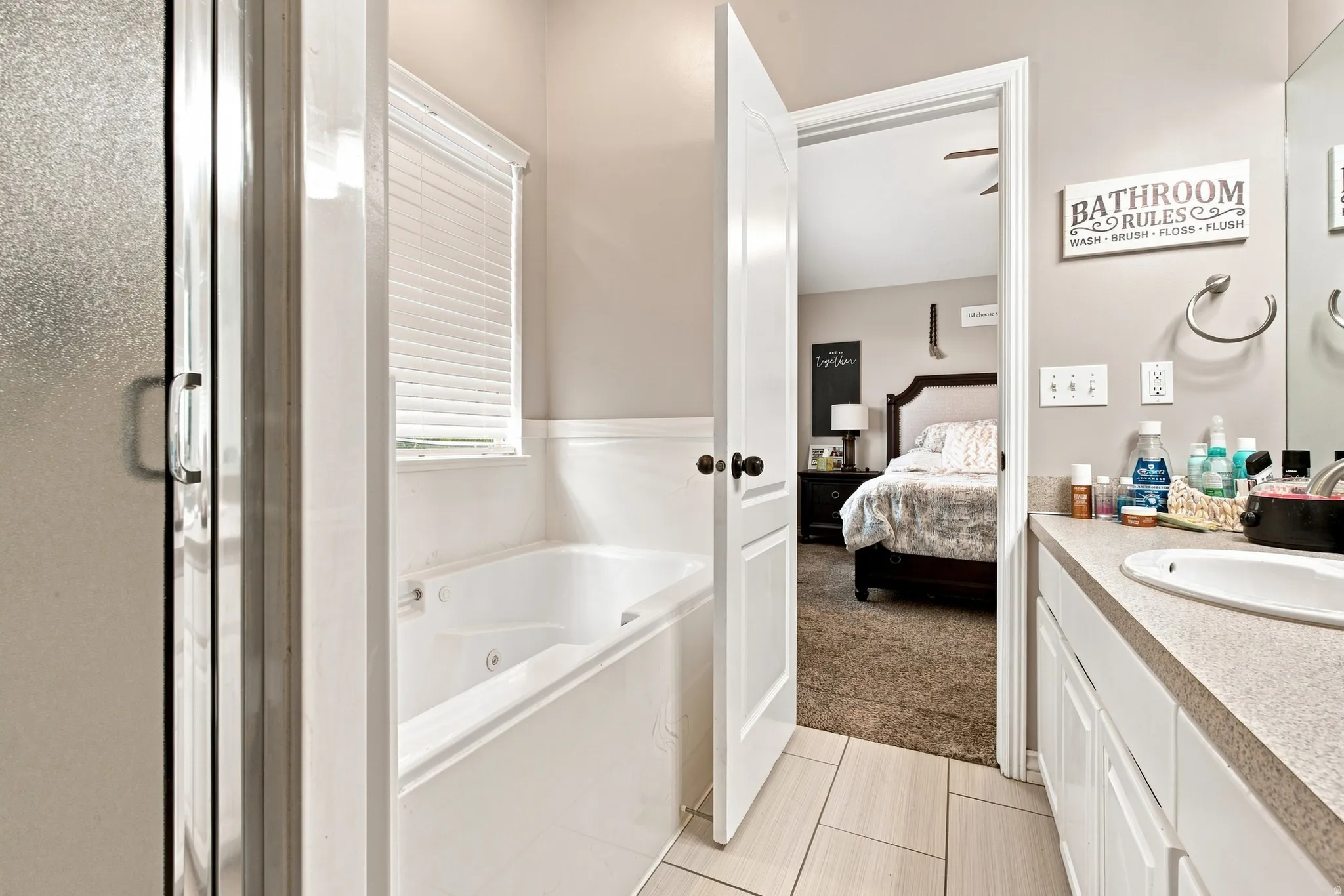 Master bathroom suite featuring a soaking tub with integrated shower enclosure, dual-sink vanity with quartz countertop, tile flooring, and direct access to the primary bedroom