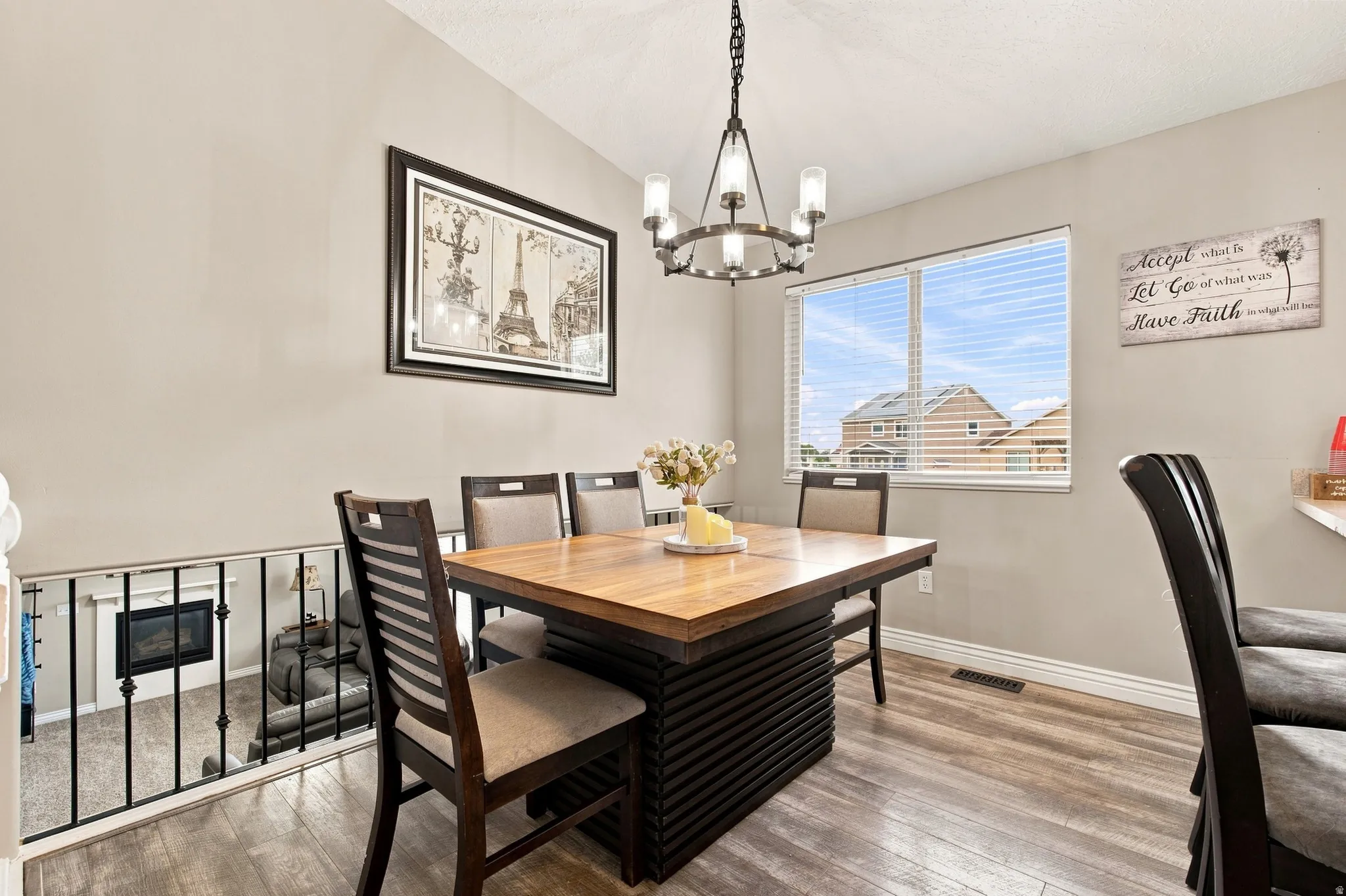 Wood-finish flooring, contemporary chandelier, large window with blinds, and a built-in fireplace feature visible from the open-concept space