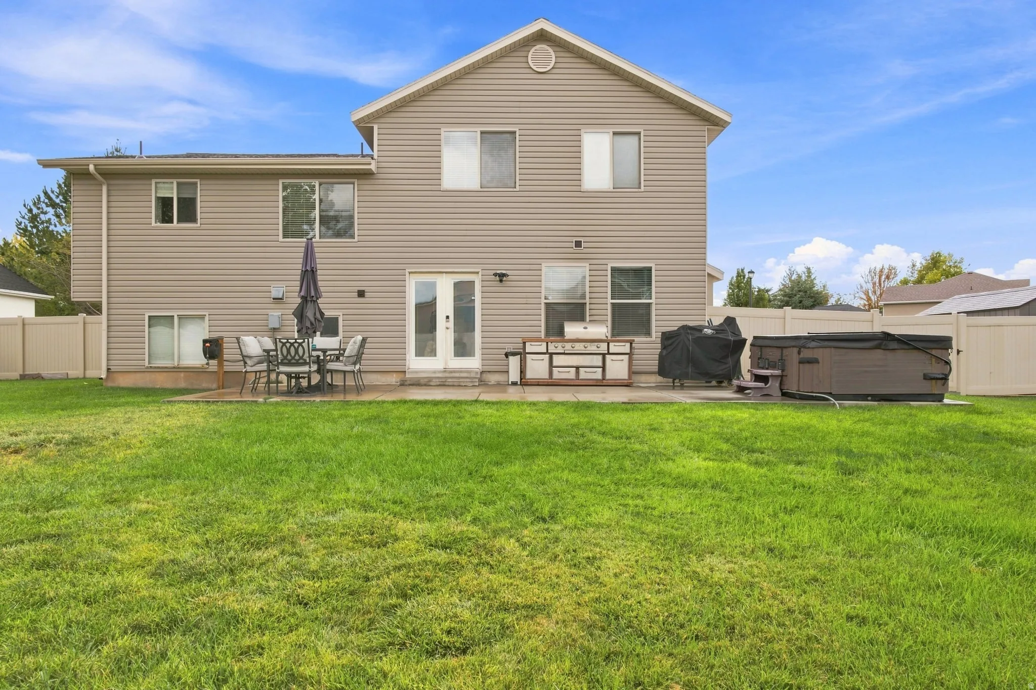 Expansive lawn area with a concrete patio, light-colored privacy fencing, and exterior siding