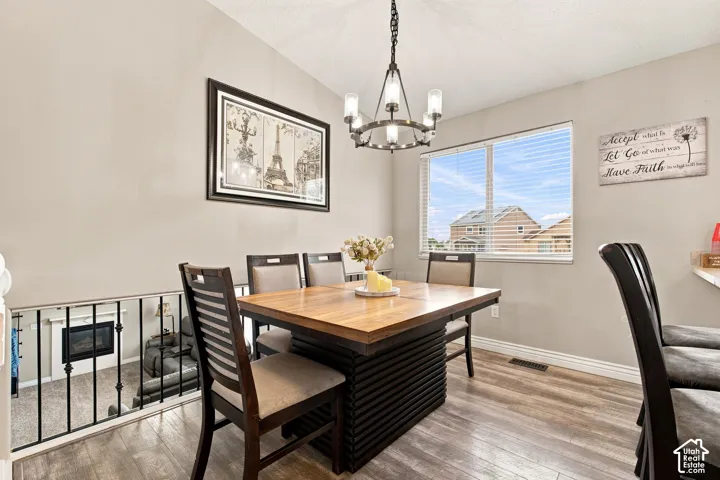 Wood-finish flooring, contemporary chandelier, large window with blinds, and a built-in fireplace feature visible from the open-concept space